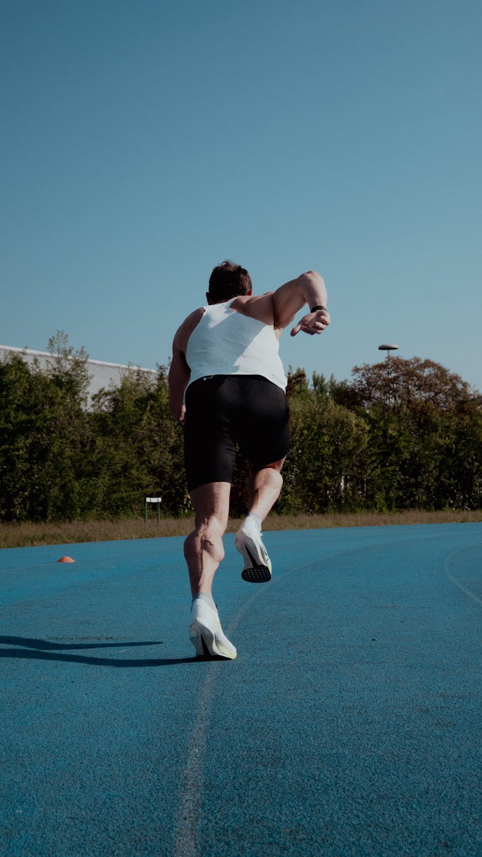 Male athlete starting a sprint on a blue outdoor track under a clear sky.