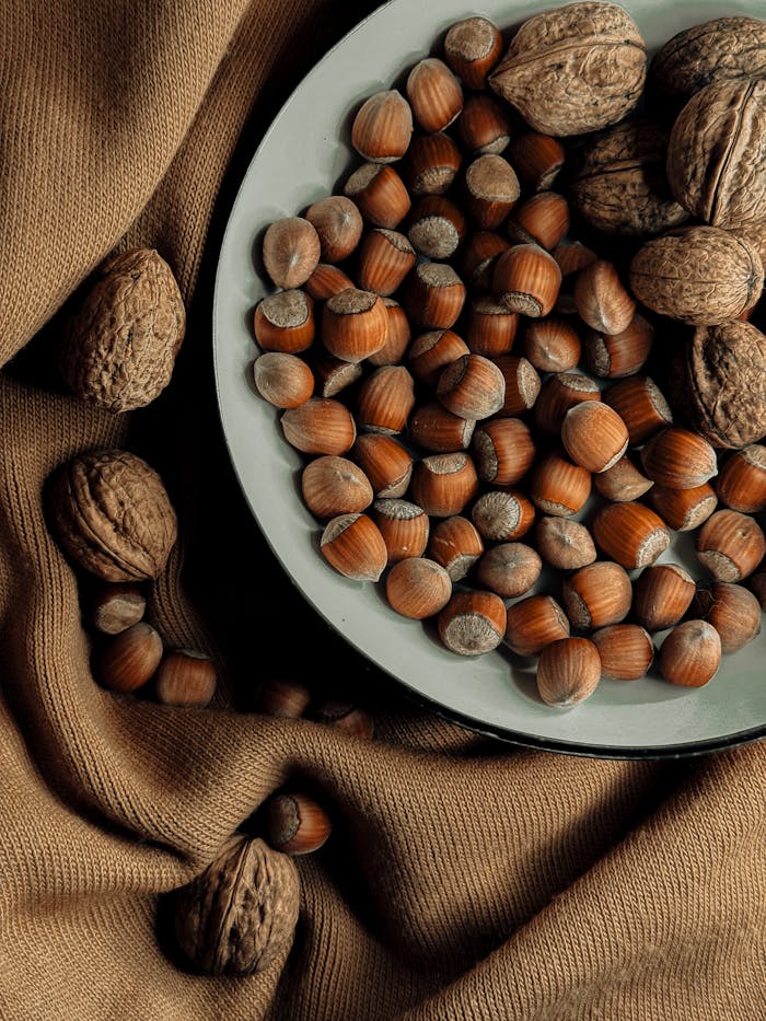 A variety of nuts including hazelnuts and walnuts on a fabric surface.