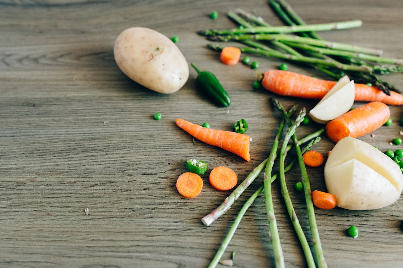 A variety of fresh organic vegetables including carrots, peas, and asparagus on a wooden surface.