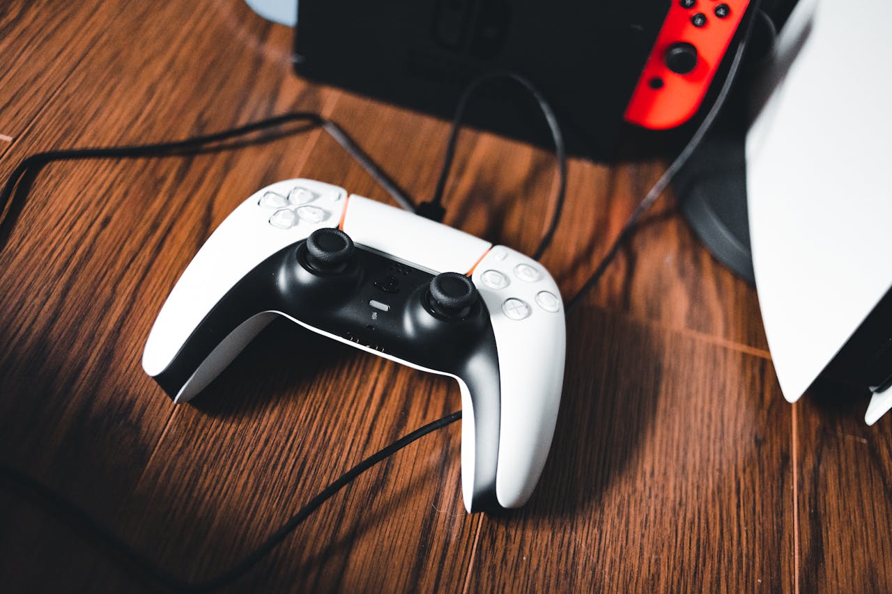 A gaming controller laying on a wooden table next to other gaming devices.